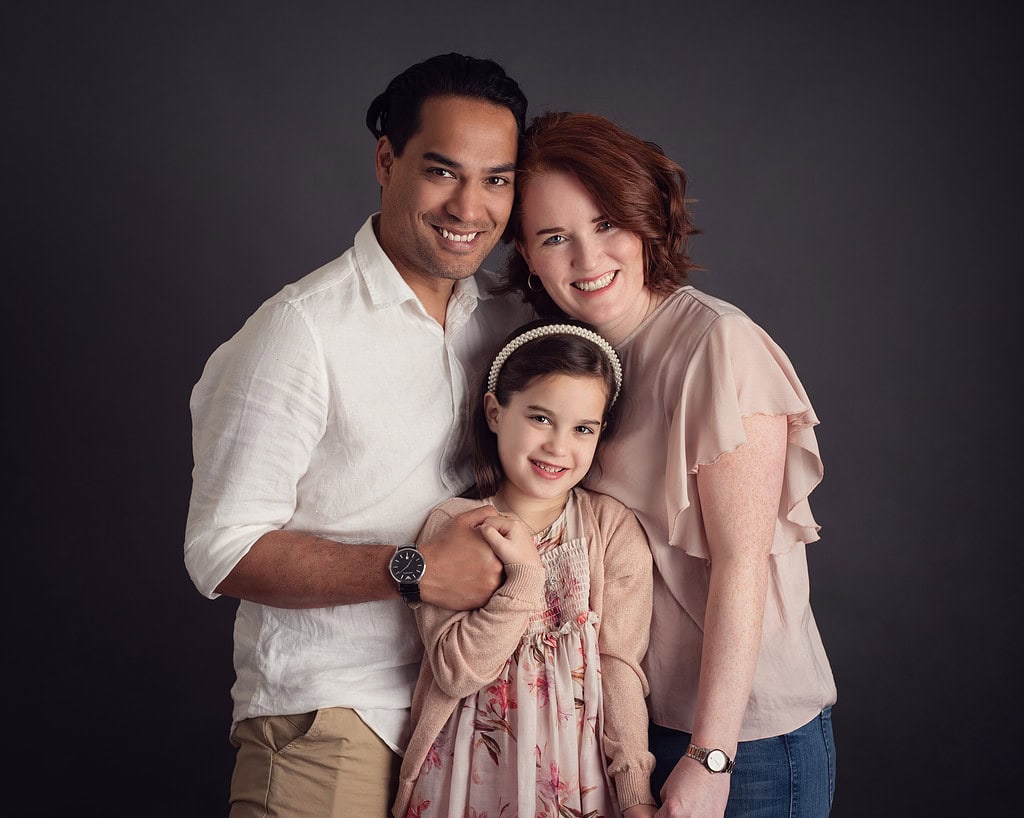 mother, father and young daughter embracing and smiling to camera