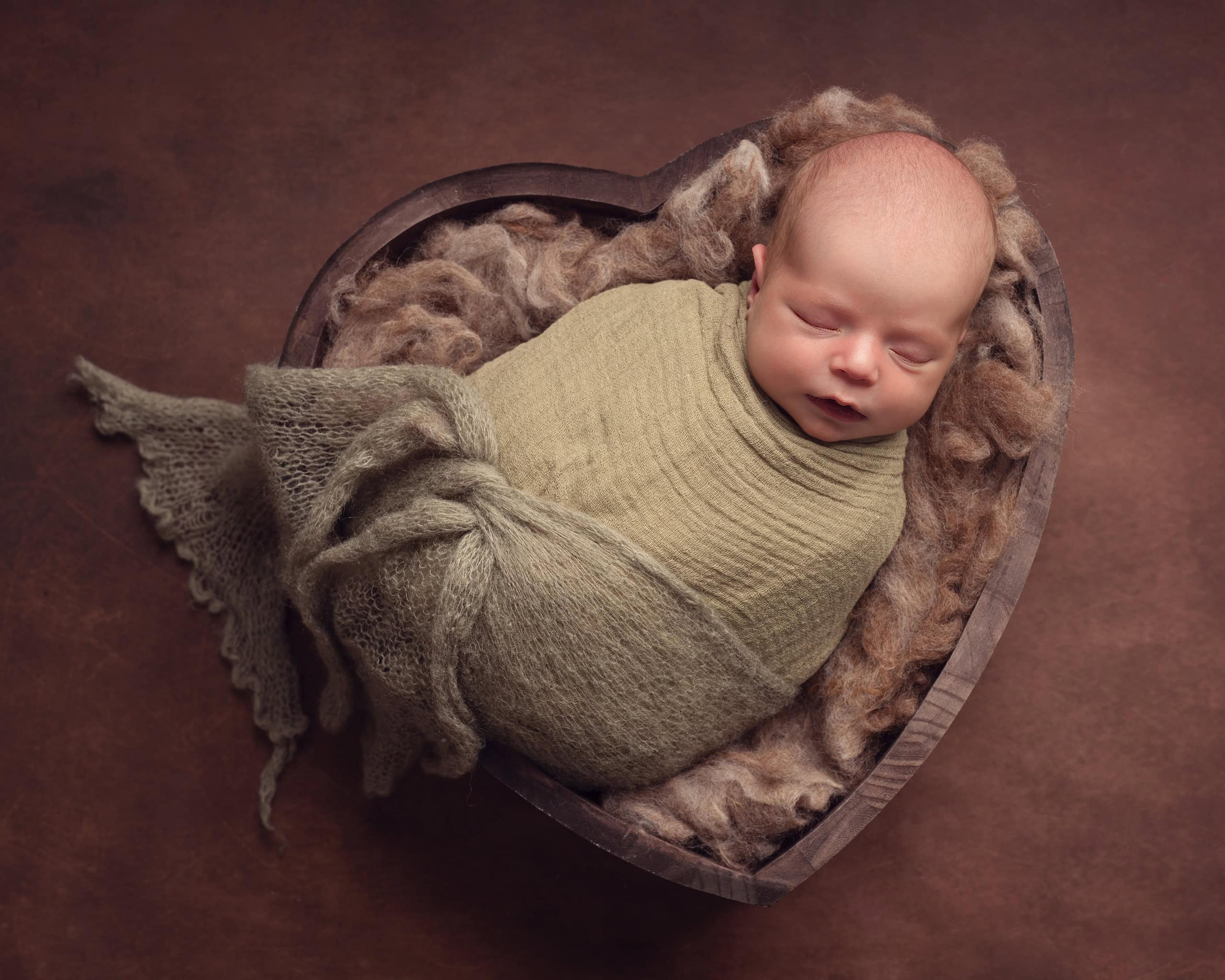 newborn baby in heart shaped bowl, brown tones