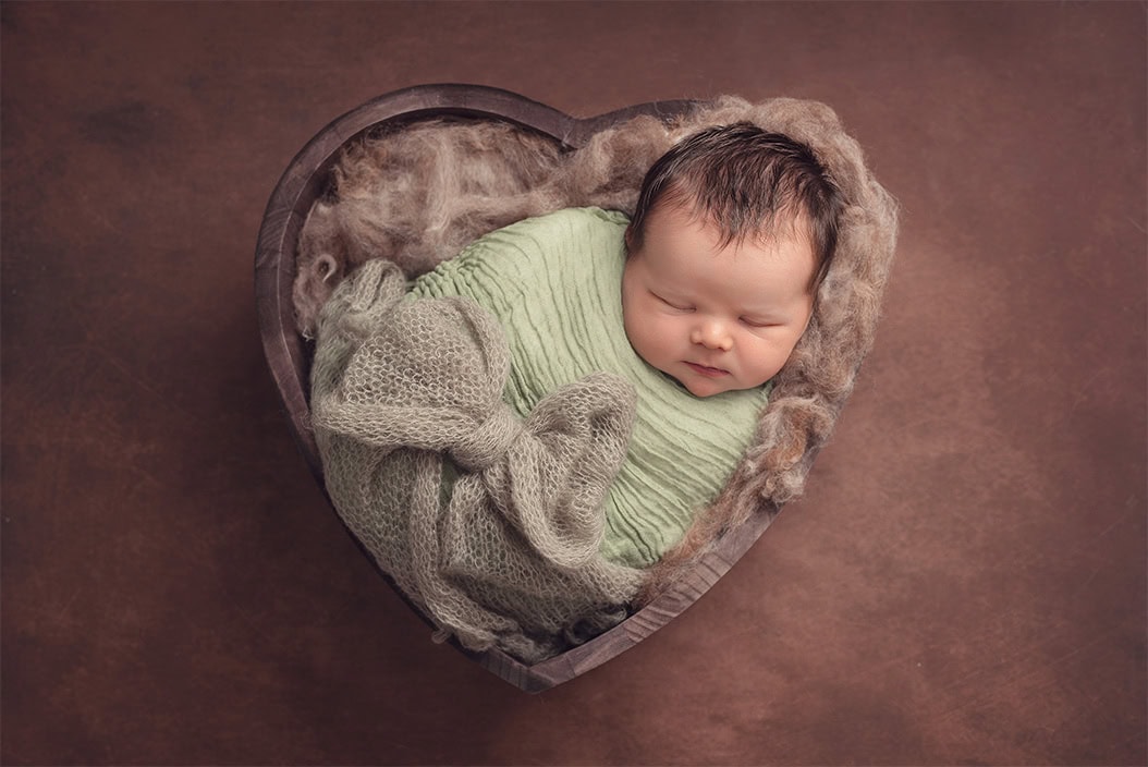 sleeping newborn baby laying in heart shaped bowl