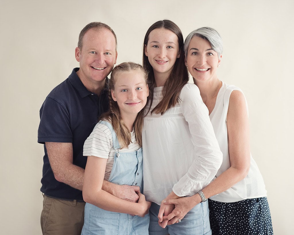 family portrait of mother, father and two teenage daughters smiling to camera