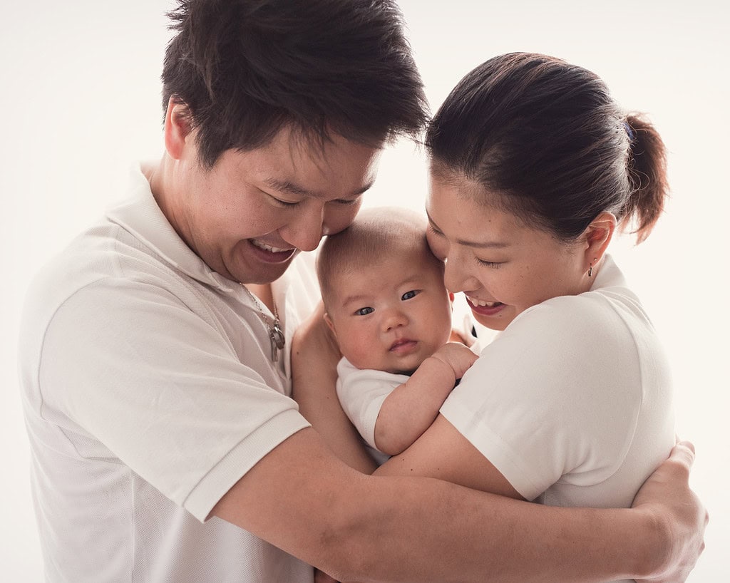 mother and father cuddling into older baby, baby looking at camera parents smiling to baby