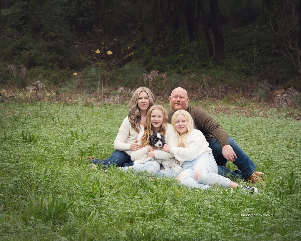 seated family portrait of mother, father two teenage daughters and a small dog set in a green grassy location