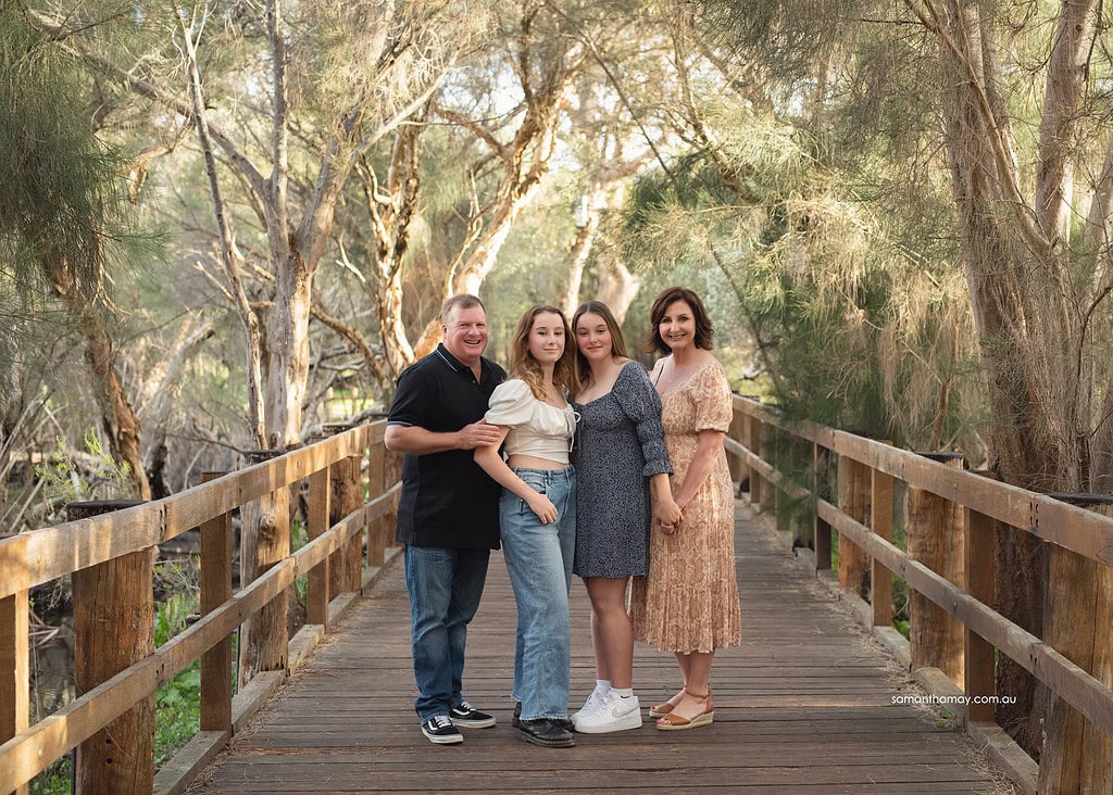 family of four with two teenage girls standing on wooden walkway in bush setting